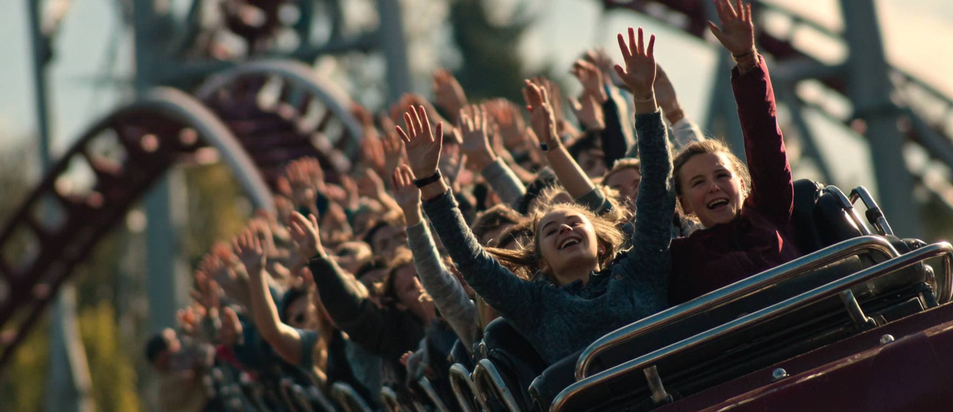 Riders throwing their hands up on a roller coaster at golden hour